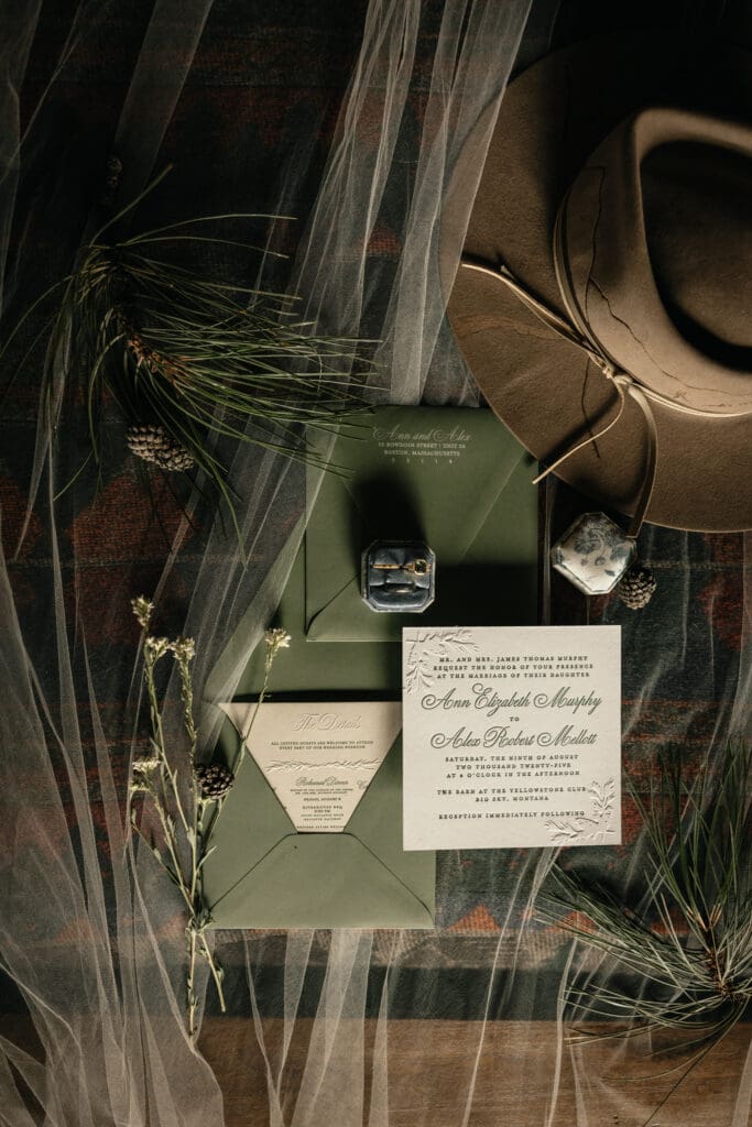 Luxury Yellowstone Club Big Sky wedding invitation suite with green envelopes, embossed letterpress details, pine accents, and western hat styling