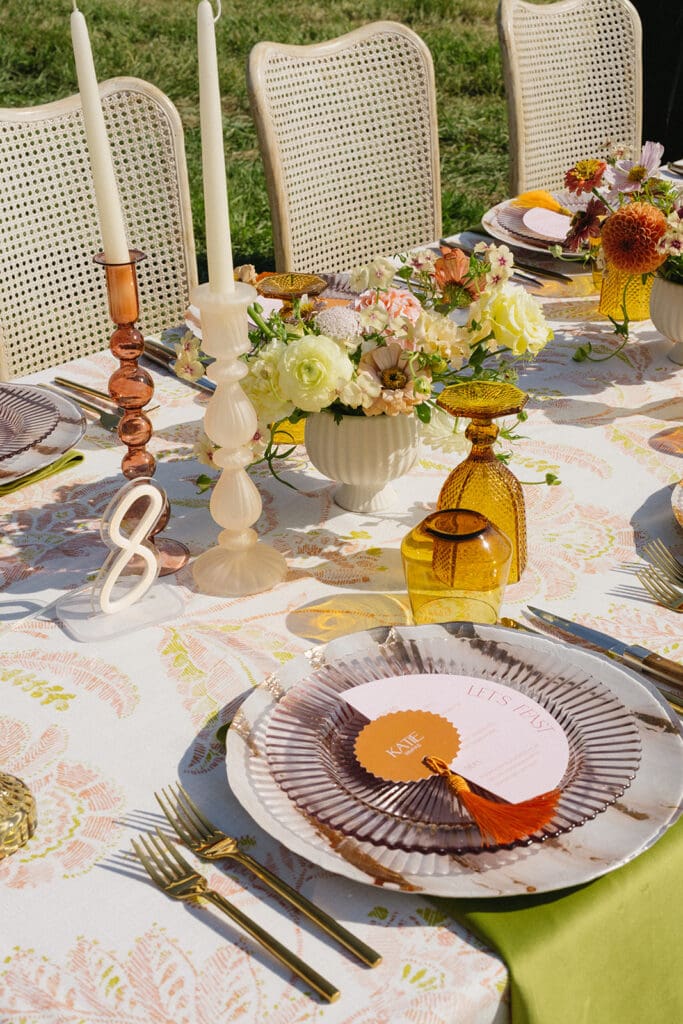 Colorful Montana wedding reception tablescape with amber glassware, patterned linens, bright floral centerpieces, and custom menu card at outdoor Bozeman wedding.