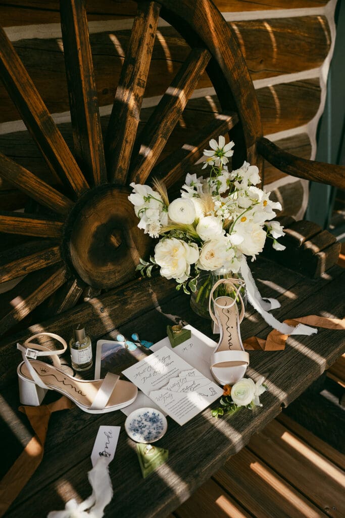 Paradise Valley, Montana wedding invitation suite styled with bridal shoes, bouquet, and western-inspired details on rustic log bench.