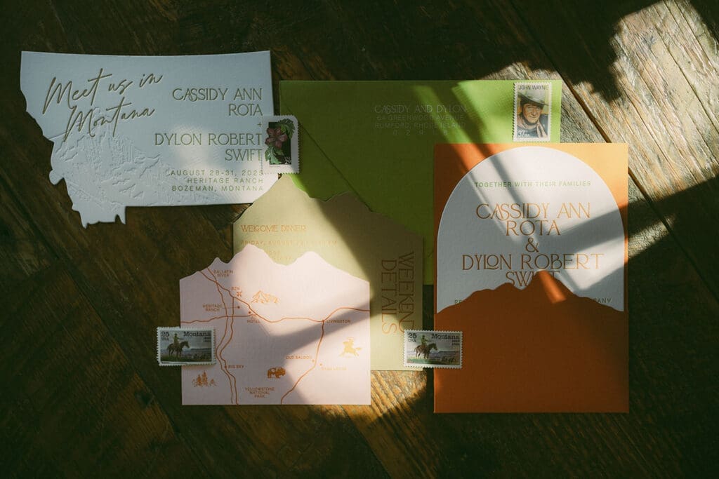 Montana-inspired wedding invitation suite featuring mountain illustration, warm sunset tones, custom map insert, and vintage Montana postage stamps for Bozeman wedding.